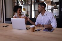 Vista frontal de personas de negocios de raza mixta que interactúan entre sí en la oficina moderna mientras se estrechan la mano con la pantalla digital en primer plano - foto de stock