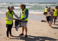Вид спереду групи з багатьох етнічних добровольців, які прибирають пляж у сонячний день — стокове фото