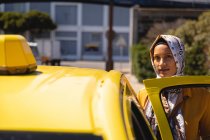 Vue de face de femme métissée réfléchie regardant la caméra tout en prenant le taxi dans la rue — Photo de stock