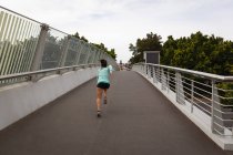 Visão traseira da jovem mulher de raça mista correndo em uma passarela na cidade — Fotografia de Stock