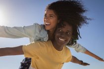 Niedrigwinkel-Ansicht junger afrikanisch-amerikanischer Mann gibt schöne junge afrikanisch-amerikanische Frau huckepack am Strand an sonnigen Tag — Stockfoto