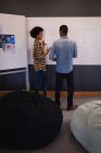 Visão traseira de jovens empresários mestiços interagindo uns com os outros no projeto sobre quadro branco em pé no escritório moderno — Fotografia de Stock