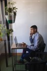 Вид сбоку на молодого бизнесмена смешанной расы, разговаривающего по мобильному телефону, используя ноутбук в современном офисе с заводами перед ним — стоковое фото