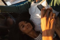 Hochwinkel-Ansicht junger afrikanisch-amerikanischer Mann fährt, während ziemlich gemischte Rennfrau Handy im Auto benutzt — Stockfoto