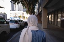Вид ззаду жінки з хіджабом, що йде на вулиці в сонячний день — стокове фото
