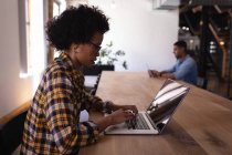 Вид збоку молодих бізнесменів змішаної раси, які працюють над ноутбуком за столом, сидячи в сучасному офісі — стокове фото