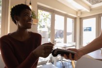 Вид збоку красива молода афроамериканець жінка робить оплату за допомогою кредитної картки в кафе — стокове фото