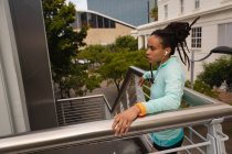 Vista laterale della giovane donna di razza mista che ascolta musica sugli auricolari sulle scale della città — Foto stock