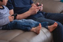 Seção média de pai e filho asiático jogando videogames juntos enquanto sentados no sofá em casa — Fotografia de Stock