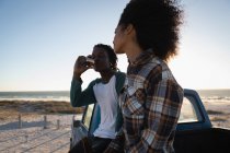 Seitenansicht eines glücklichen jungen afrikanisch-amerikanischen Paares, das an einem sonnigen Tag Bier im Auto am Strand trinkt — Stockfoto