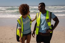 Вид спереди двух счастливых мультиэтнических добровольцев, взаимодействующих друг с другом на пляже — стоковое фото