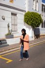 Vue de face de la femme de race mixte utilisant un téléphone portable tout en marchant dans la rue par une journée ensoleillée — Photo de stock