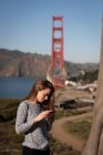 Вид збоку красивої жінки, що використовує мобільний телефон, стоячи — стокове фото