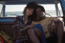 Vista frontal de la joven pareja romántica afroamericana sentada en coche en la playa en un día soleado - foto de stock