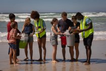 Vista frontal de un grupo joven de voluntarios multiétnicos limpiando la playa en un día soleado - foto de stock