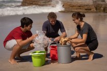 Front view of group of multi ethnic volunteers cleaning beach while sitting in squat position in front of buckets on a sunny day — Stock Photo