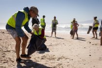 Vista frontale del gruppo di volontari multietnici che puliscono la spiaggia in una giornata di sole — Foto stock