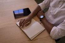 Высокий угол обзора вдумчивого бизнесмена, сидящего за деревянным столом с ноутбуком, ручкой и цифровой планшетом — стоковое фото