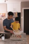 Vista frontal de padre e hijo asiáticos mezclando masa juntos en la cocina en casa - foto de stock
