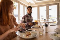 Side view of mixed race female friends interacting with each other while having breakfast in restaurant — Stock Photo