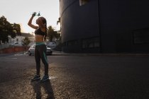 Vista laterale della vestibilità giovane donna di razza mista versando acqua sulla testa in strada — Foto stock