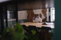 Вид спереду молодого бізнесмена змішаної раси, який працює над ноутбуком за столом в сучасному офісі — стокове фото
