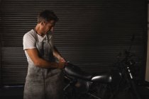 Vue de face du mécanicien de vélo masculin caucasien fixant le vélo et portant un tablier dans le garage — Photo de stock