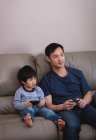Вид з днем азіатських батько і син грають разом на відеоігри, сидячи на дивані будинку — стокове фото