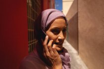 Vista frontal da bela mulher de raça mista falando no telefone celular enquanto estava em pé no beco em um dia ensolarado — Fotografia de Stock