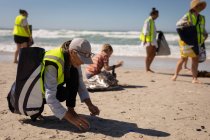 Вид спереду багато етнічних добровольців, які прибирають пляж у сонячний день — стокове фото