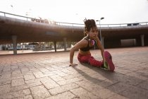 Вид спереду підходить молодій змішаної раси жінка робить вправи на розтяжці на вулиці — стокове фото