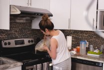 Vista trasera de la mujer asiática vertiendo la mezcla de panqueques en una sartén en la cocina en casa - foto de stock