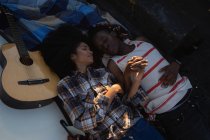Высокоугольный вид молодой афроамериканской пары, лежащей в машине возле гитары на пляже в солнечный день — стоковое фото