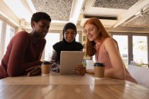 Frontansicht von jungen Freundinnen gemischter Rassen, die miteinander interagieren, während sie digitale Tablets in einem Café benutzen — Stockfoto