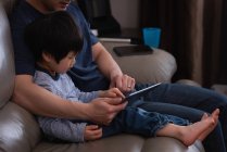 Вид збоку азіатського батька і його сина за допомогою цифрової таблетки, сидячи на дивані вдома — стокове фото