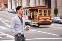 Вид на красивий Азіатська людина, що стоїть на вулиці, коли з кавою — стокове фото