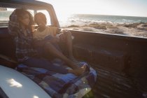 Vista lateral de la joven pareja afroamericana interactuando entre sí mientras están sentados en el coche en la playa en un día soleado - foto de stock