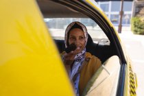 Vista frontal de la hermosa mujer de raza mixta hablando por teléfono móvil mientras viaja en coche en un día soleado - foto de stock