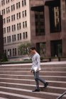 Вид збоку красивий Азіатська людина, що йде з сходів при проведенні цифрової таблетки — стокове фото