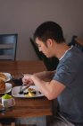 Vista lateral de um homem asiático tomando café da manhã na mesa de jantar na cozinha em casa — Fotografia de Stock