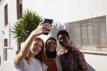 Front view of happy mixed race female friends taking selfie at city street — Stock Photo