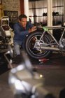 Vista frontal del mecánico de bicicleta masculino caucásico que fija el nuevo asiento en moto en el garaje - foto de stock