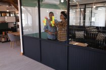 Vue de face des jeunes gens d'affaires métis écrivant sur des notes collantes dans un bureau moderne — Photo de stock