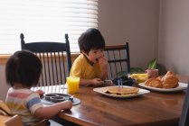 Вид спереди азиатских детей, завтракающих, сидя за обеденным столом на кухне дома — стоковое фото