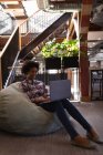 Вид сбоку красивой бизнесвумен смешанной расы, использующей ноутбук, расслабляясь в офисе на фоне лестницы на заднем плане — стоковое фото