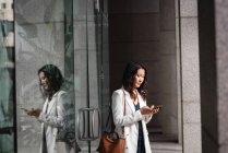 Vista lateral da mulher asiática usando telefone celular enquanto está em pé no corredor — Fotografia de Stock