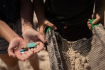 Sección media de voluntarios con residuos en la mano en la playa en un día soleado - foto de stock