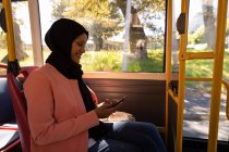 Vue latérale d'une belle femme métissée souriante et utilisant son téléphone portable en voyage en bus — Photo de stock