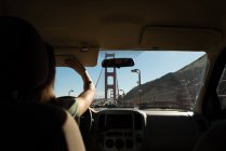 Mujer conduciendo coche sobre puente de puerta de oro en un día soleado - foto de stock