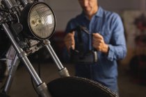 Fechar a luz da cabeça da bicicleta com mecânico de bicicleta masculino no fundo na garagem — Fotografia de Stock